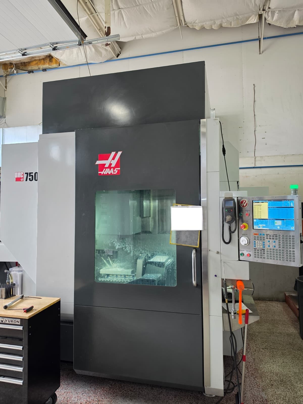 Haas UMC-750 5-axis machining center cutting a part, coolant on the enclosure window